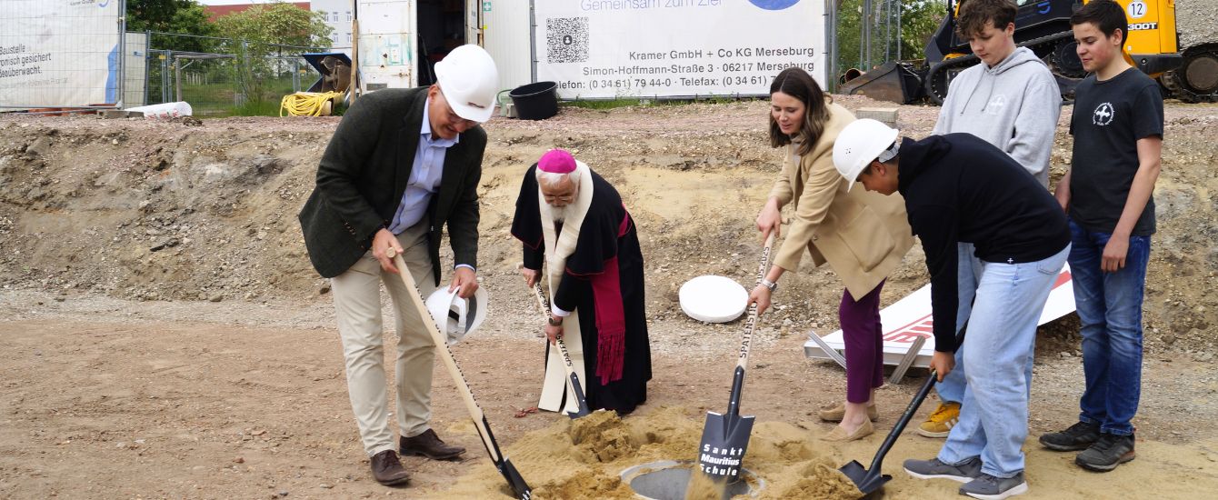 Bischof Feige und weitere Personen auf der Baustelle beim Spatenstich