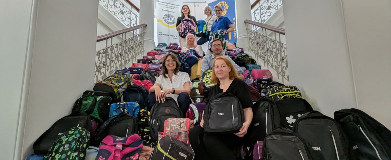 Menschen zeigen sich mit gesammelten Schulranzen auf einer Treppe