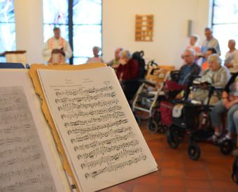Im Vordergrund ein Notenständer, im Hintergrund die Gemeinde beim Gottesdienst