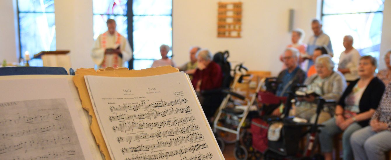 Im Vordergrund ein Notenständer, im Hintergrund die Gemeinde beim Gottesdienst