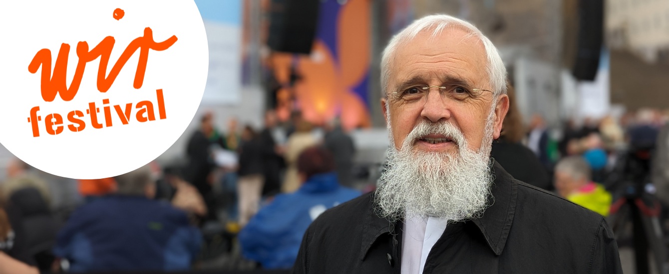 Bischof Feige neben dem Logo des WIR-Festivals