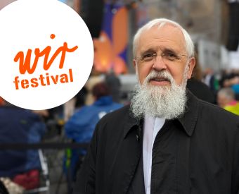 Bischof Feige neben dem Logo des WIR-Festivals