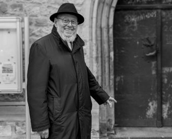 Schwarz-weiß Bild eines Geistlichen vor einer Kirchentür