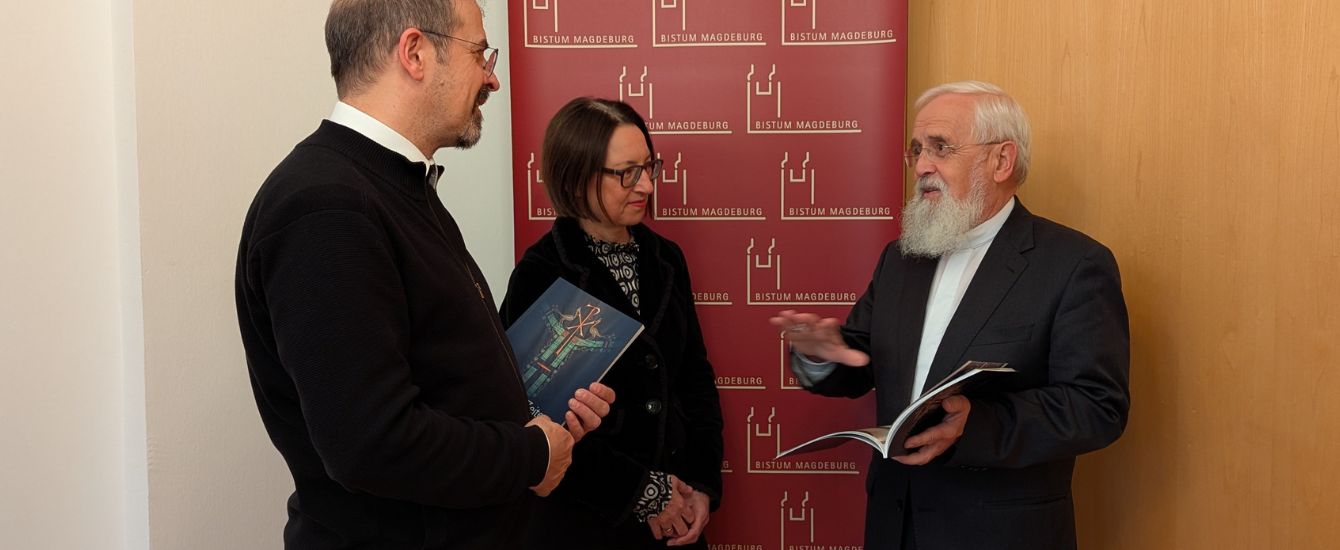 Bischof Feige spricht mit zwei Mitarbeitern über ein Buch