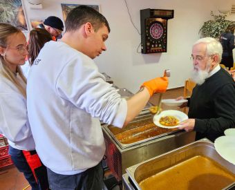 Bischof Feige lässt Essen auf zwei Teller füllen, um es zu verteilen