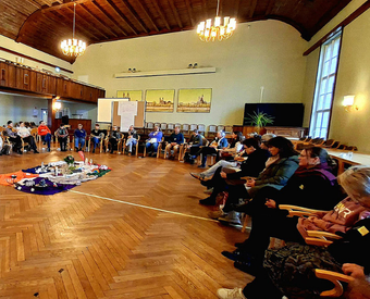 Eine Gruppe Menschen sitzt in einem großen Kreis in einem großen Saal.