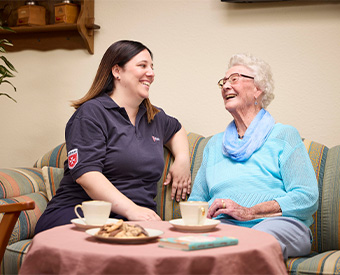 Maltesermitarbeiterin sitzt neben einer lachenden Rentnerin