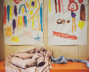 Eine Jacke und ein Schal liegen unter Kinderbildern auf einer Umkleidebank.