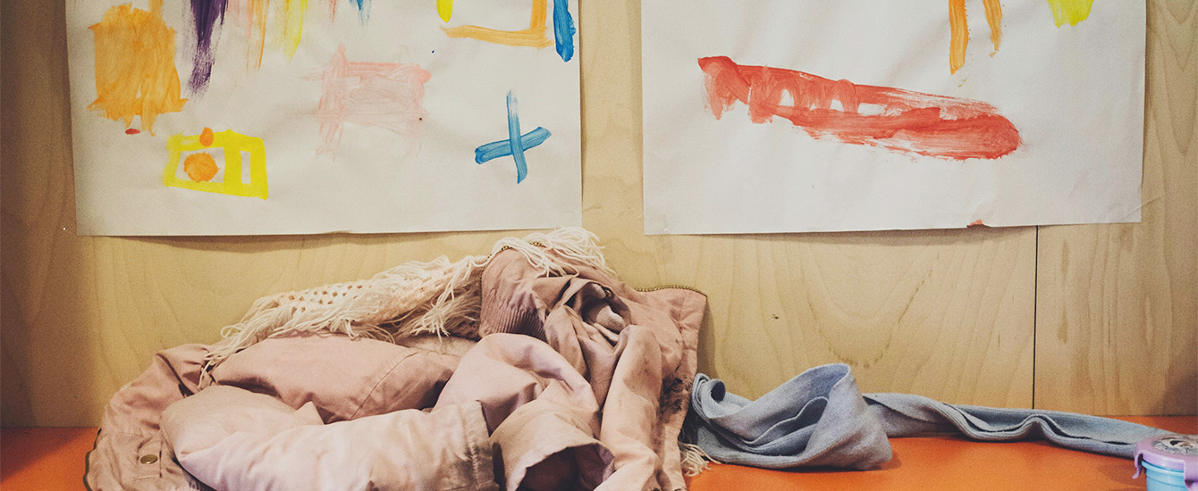 Eine Jacke und ein Schal liegen unter Kinderbildern auf einer Umkleidebank.