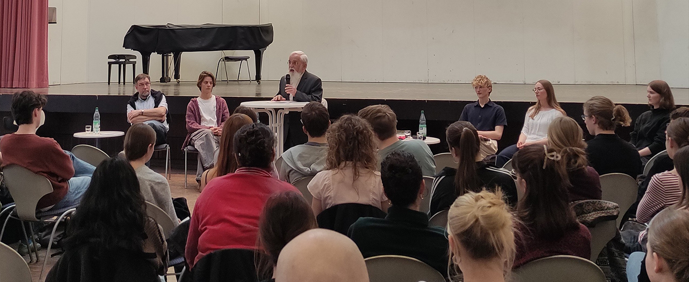 Schülerinnen und Schüler in einer Gruppe, vor ihnen ein Mann mit Mikrofon