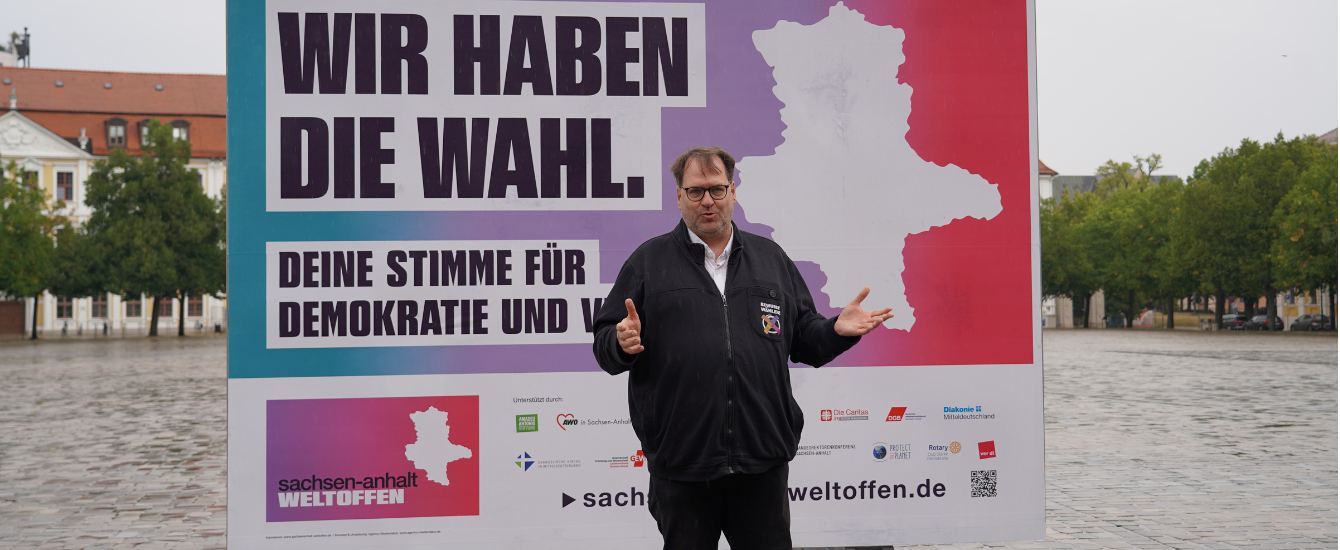 EIn Mann steht vor einem Plakat