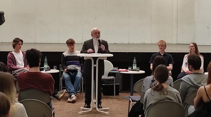 Bischof Feige mit Mikrofon vor Schülerinnen und Schülern