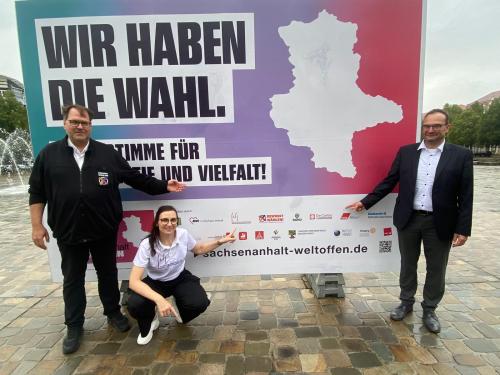 drei Menschen vor einem Plakat