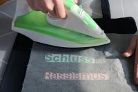 Mit dem Bügeleisen wird der Schriftzug "Schluss mit Rassismus" von einer Transferfolie auf ein T-Shirt übertragen.