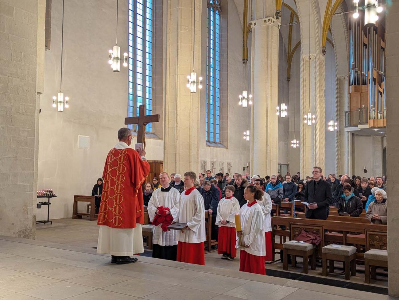 EIn Diakon hält das enthüllte Kreuz vor der Gemeinde