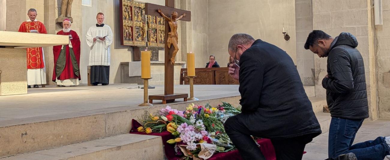 Menschen knien vor einem Kreuz