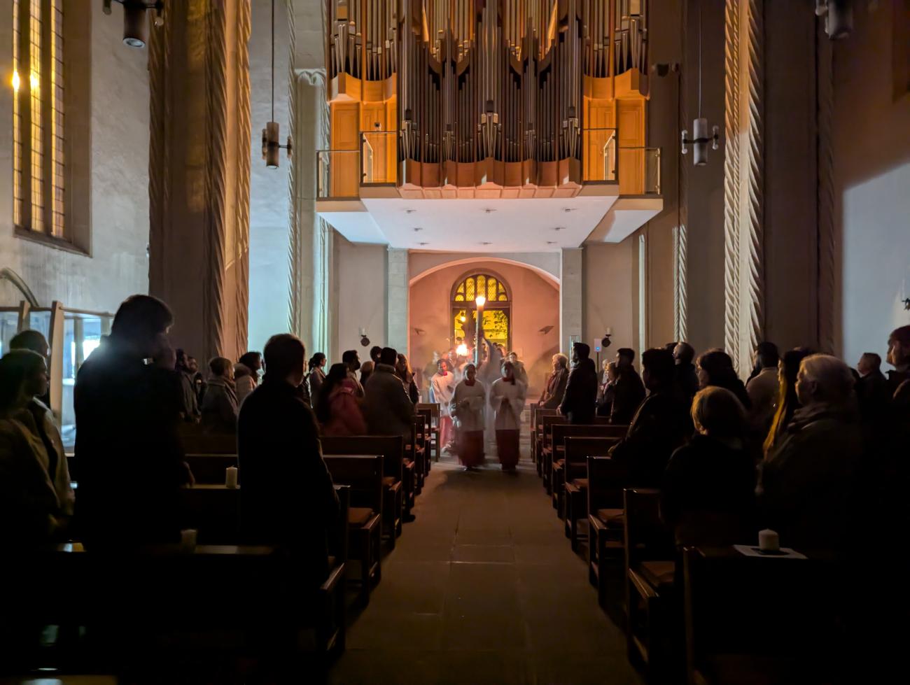 Priester ziehen mit einer Kerze in eine dunkle Kirche ein
