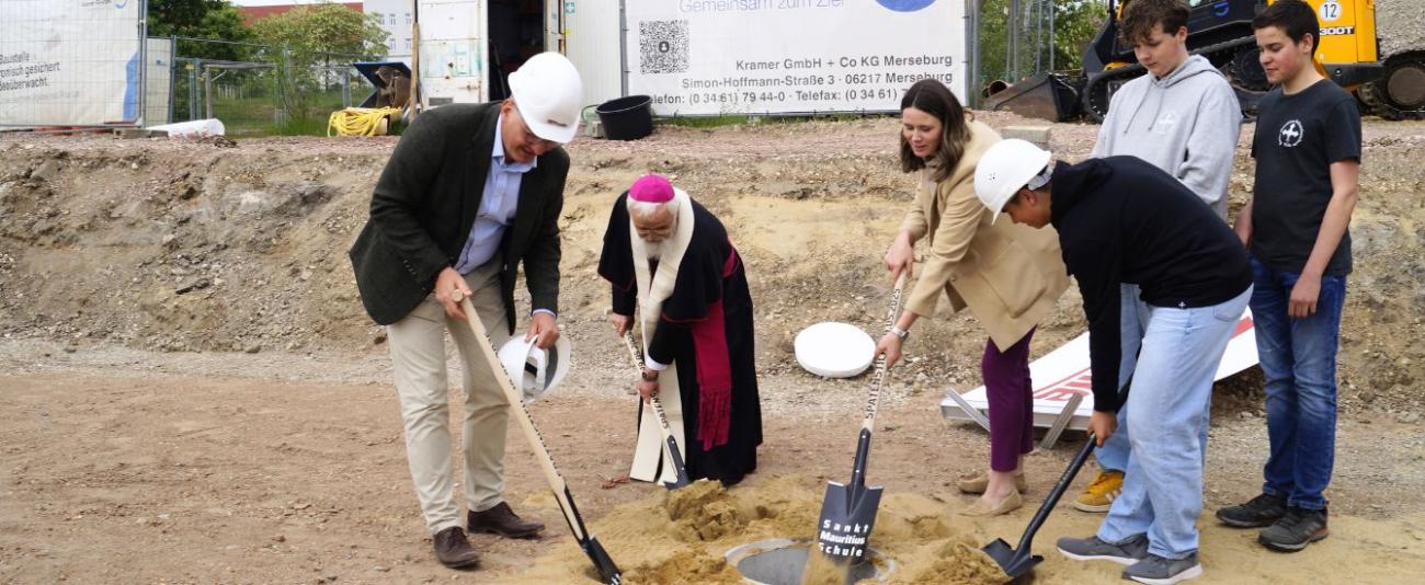 Bischof Feige und weitere Personen auf der Baustelle beim Spatenstich