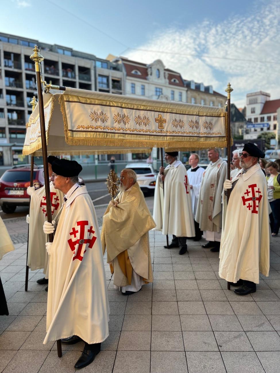 Kleriker und Gläubige laufen mit einem Baldachin durch eine Stadt