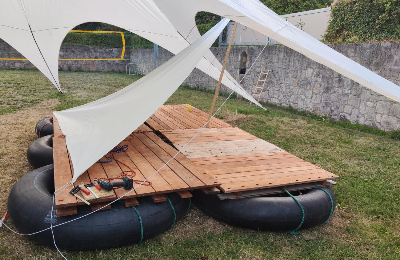 Ansicht Floßbau, große Gummireifen, Holzplatten, Seile und Sonnensegel.