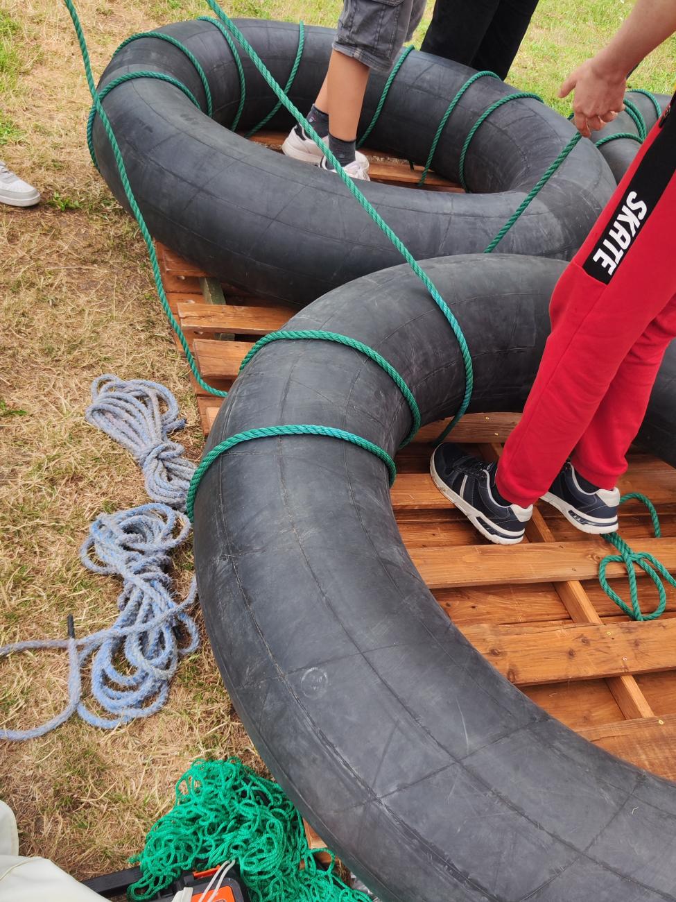 Ansicht Floßbau, große Gummireifen, Holzplatten und Seile.