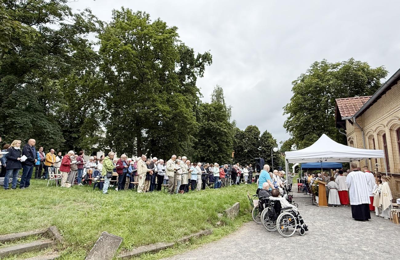 Gläubige sitzen im Garten auf Bänken und hören die Predigt