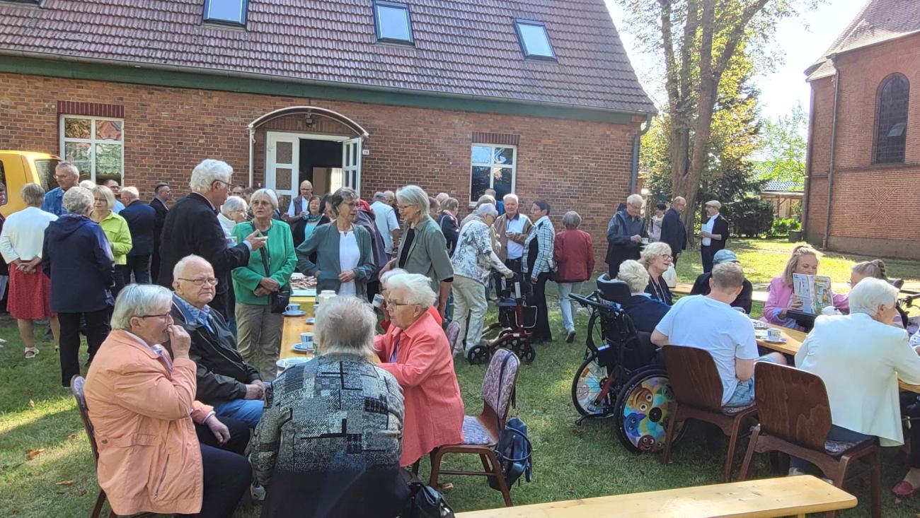 Menschen sitzen an Tischen in einem Garten