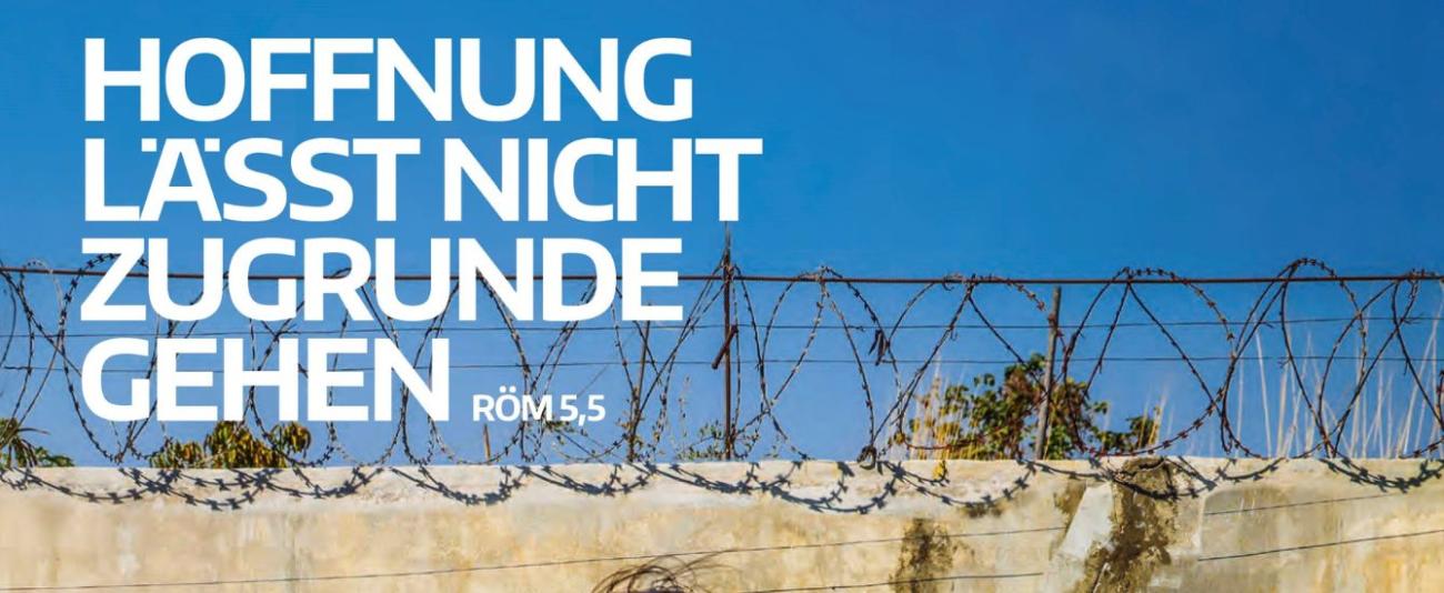 Weiße Schrift, die vor einem Stacheldrahtzaun sagt: Hoffnung lässt nicht zugrunde gehen