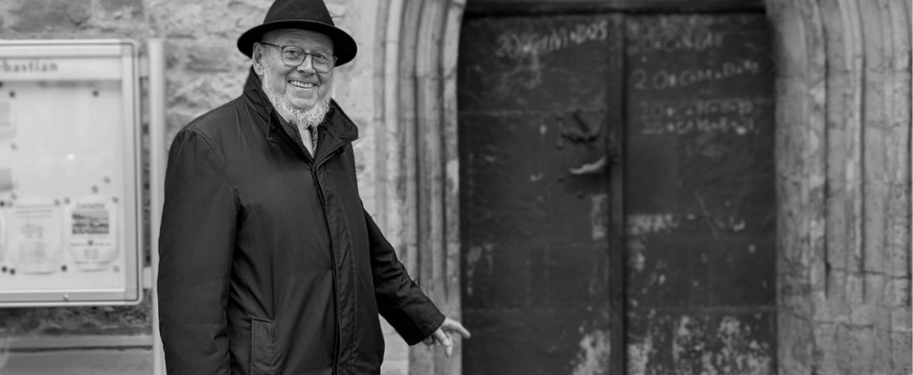 Schwarz-weiß Bild eines Geistlichen vor einer Kirchentür