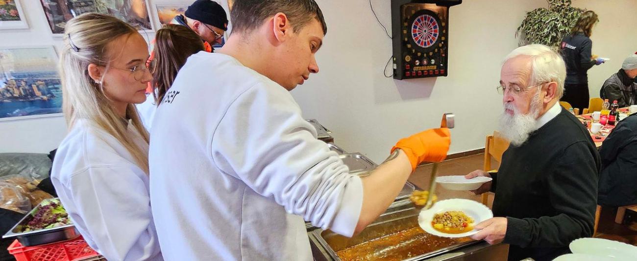 Bischof Feige lässt Essen auf zwei Teller füllen, um es zu verteilen