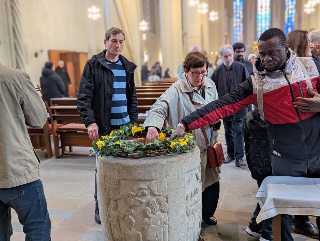 Menschen benetzen sich mit Weihwasser aus dem Taufbecken