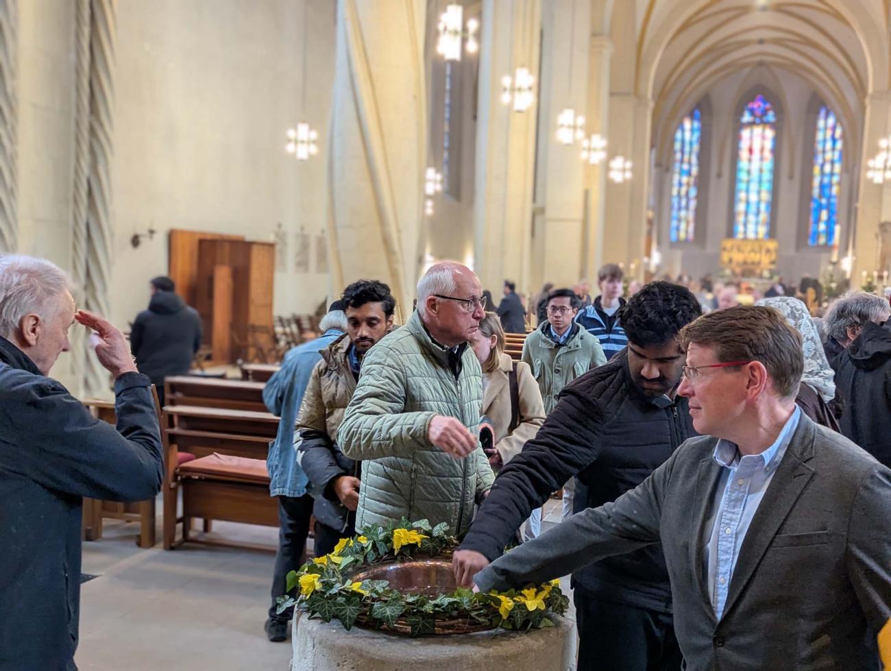 Menschen benetzen sich mit Weihwasser aus dem Taufbecken