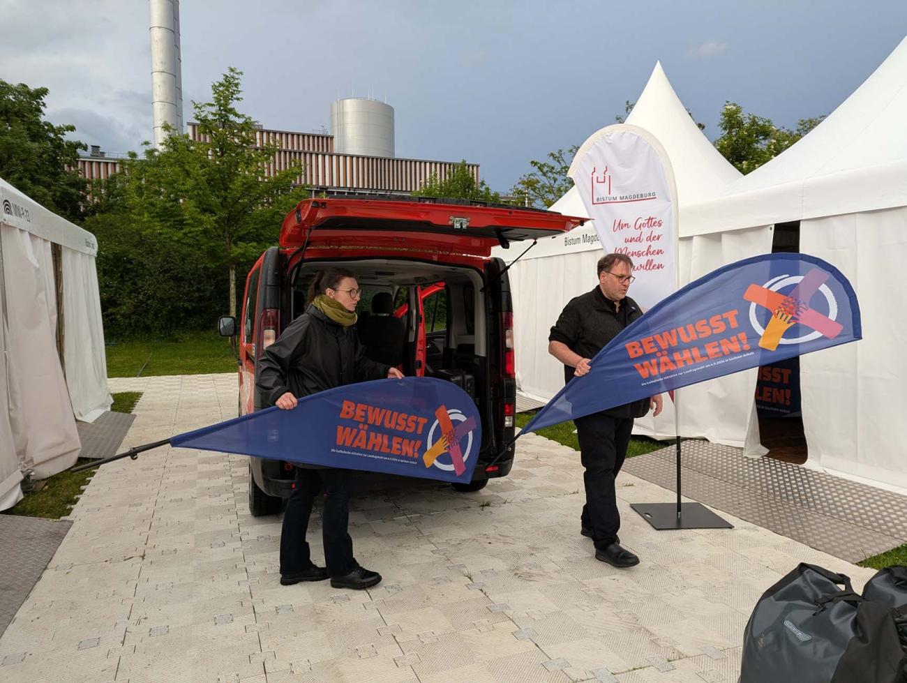 Zwei Menschen mit Fahnen in der Hand vor Zelten