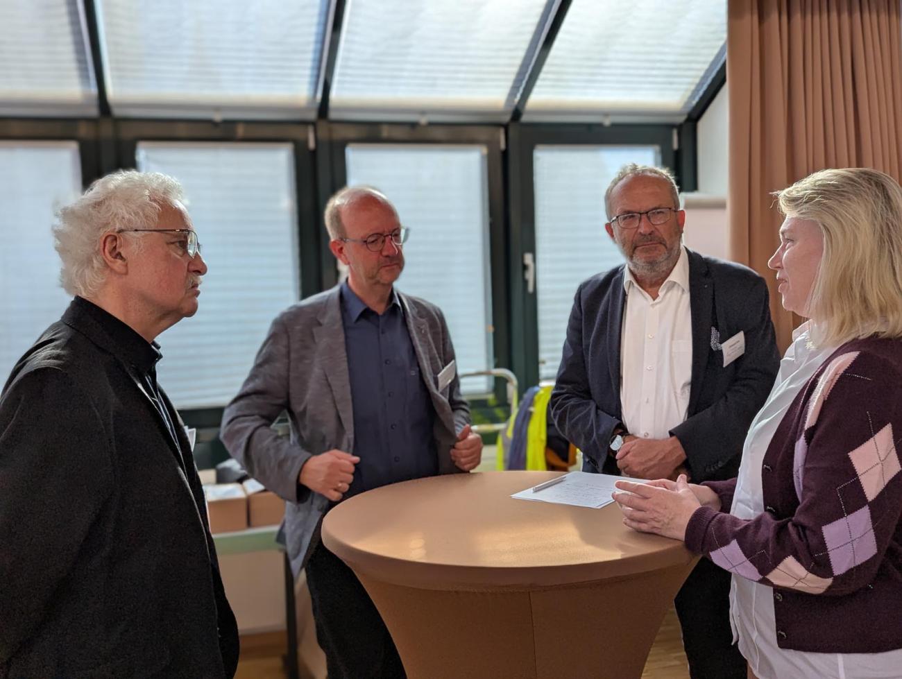 Eine kleine Gruppe an Menschen unterhält sich an einem Stehtisch
