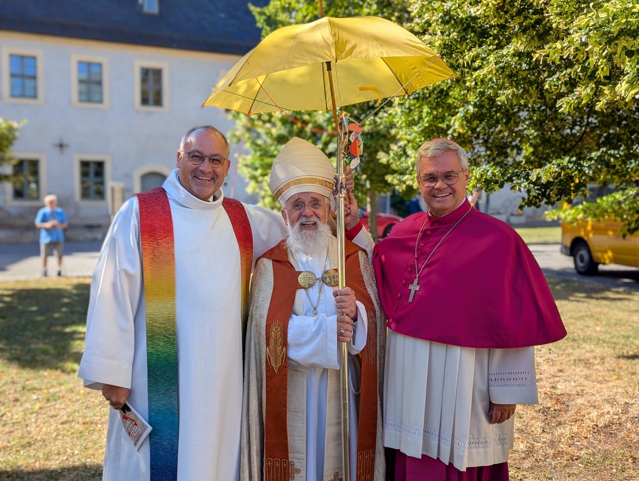 Drei Männer stehen lachend unter einem Regenschirm