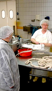 Bischof schaut sich die Wurstproduktion an.