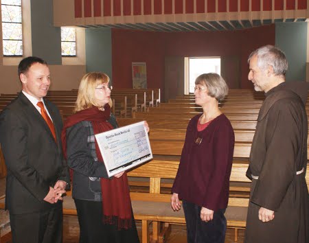 Kirchenmusikerin und Pfarrer nehmen den Scheck entgegen