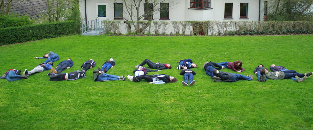 Jugendlich liegen auf der Wiese und bilden das Wort JULEICA nach.